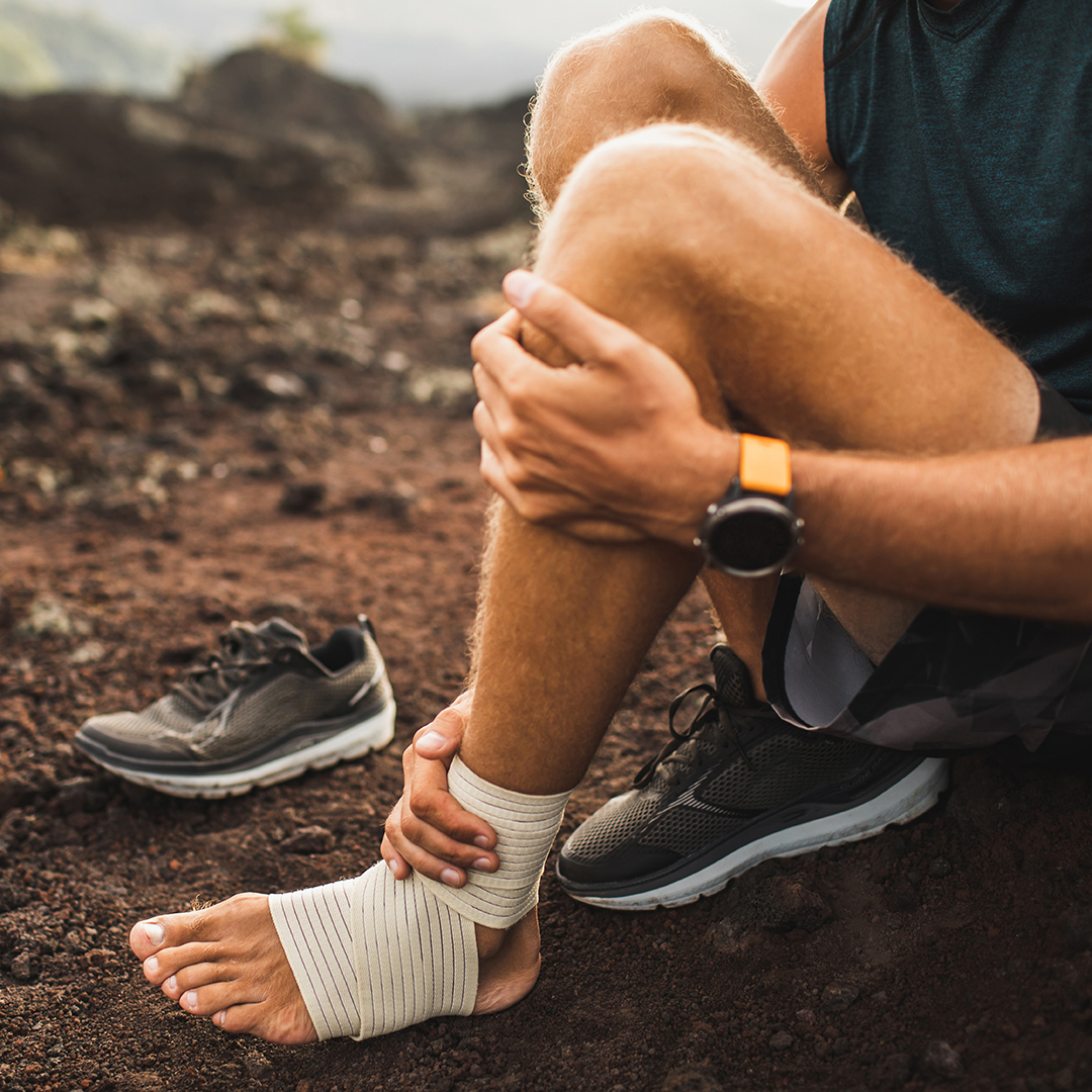 Man bandaging injured ankle. Injury leg while running outdoors. First aid for sprained ligament or tendon. Close-up on dark background.